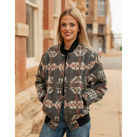 Model wearing the Sagebrush Spirit Bomber Jacket, showing the warm brown and tan Aztec pattern while posing outdoors