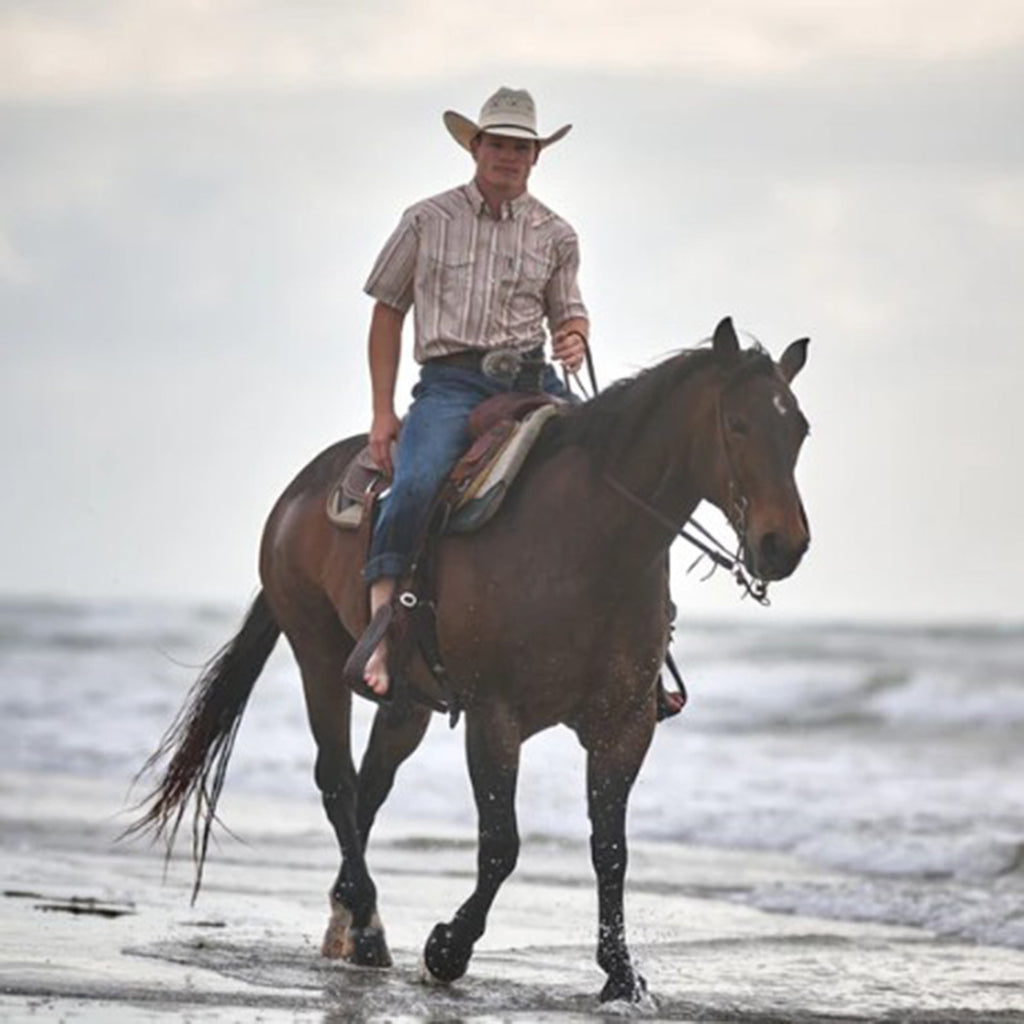 Model wearing the Sol cream striped short sleeve pearl snap shirt while sitting on a horse, showing front view and Western details.