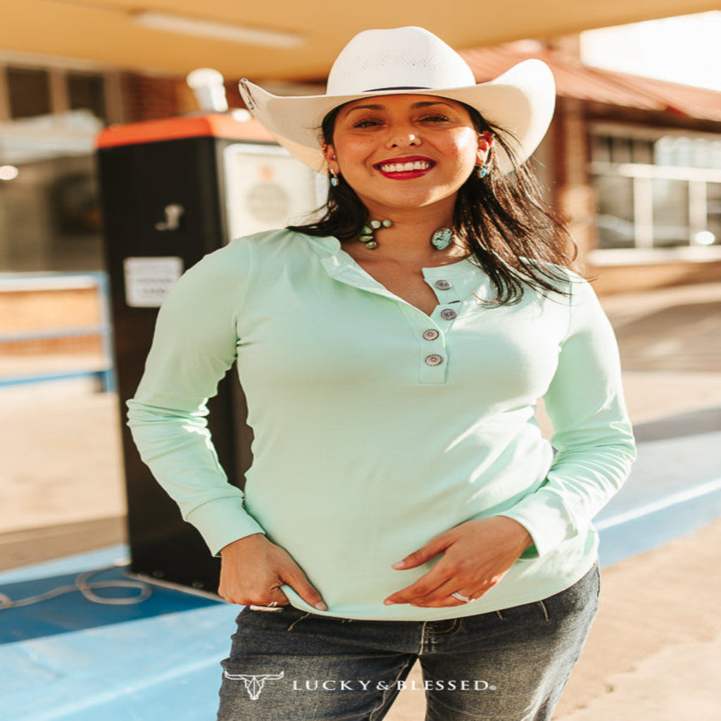 Woman wearing a mint ivory quarter-button long-sleeve shirt with a relaxed fit, styled with denim and Western-inspired accessories.