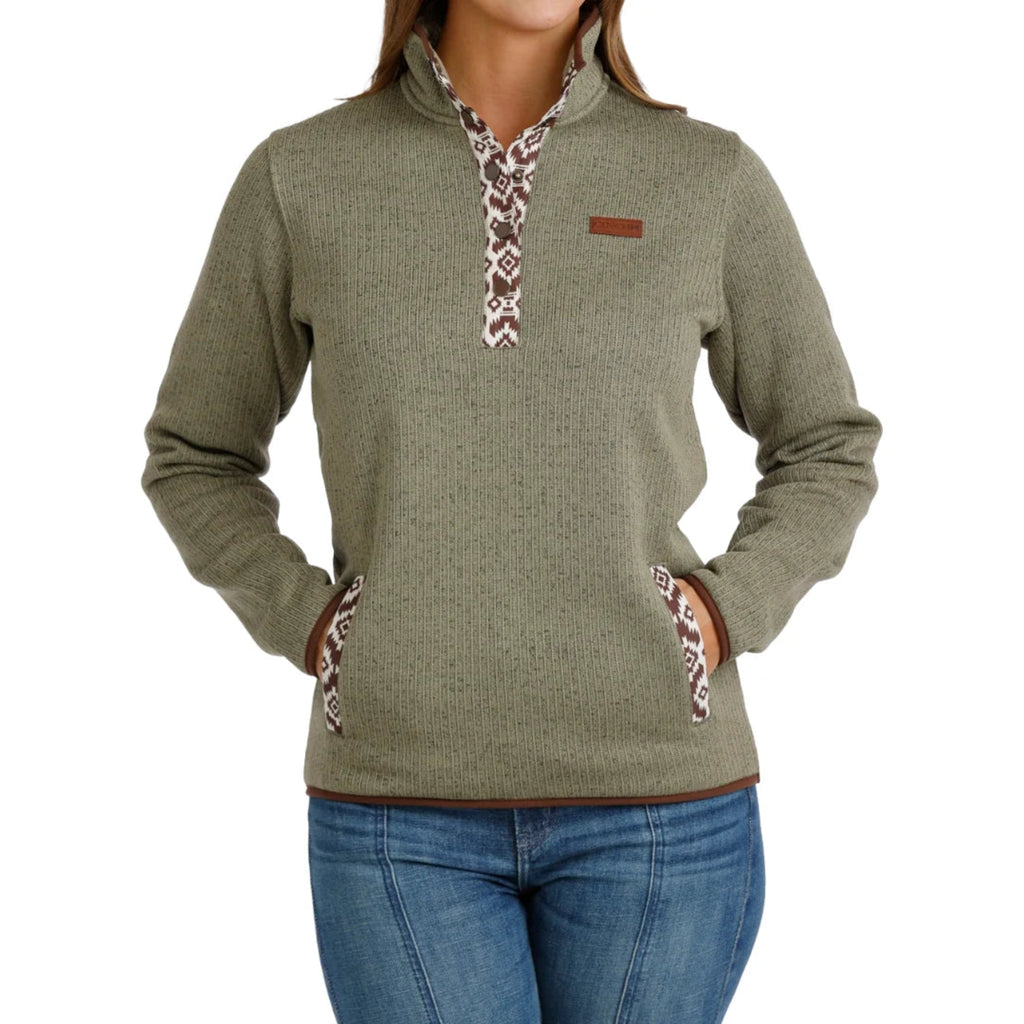 Woman wearing sage green ribbed pullover sweater with a patterned snap-placket collar and front kangaroo pockets, paired with blue jeans.