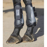 Horse legs and feet standing on dirt wearing a black protective leg boot. 