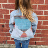 Back view of a little girl wearing a Denim Aztec Jacket, looking at a brick building.