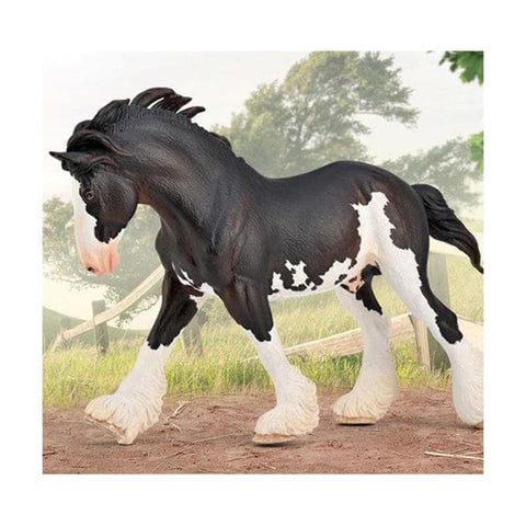 Model horse with black and white coat standing on a dirt path with greenery