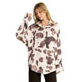 Woman wearing a cream and brown cow print long sleeve shirt with one arm raised