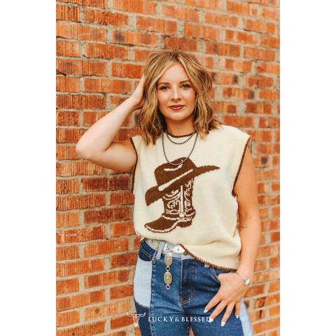 Woman wearing a sand colored sweater vest featuring a brown cowboy boot and hat.