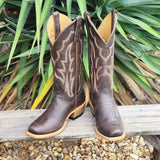 Pair of brown cowboy boots with decorative patterns on a wooden ledge with green plants in the background.