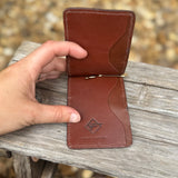 Brown leather wallet with a visible brand logo held by a hand on a wooden surface.