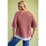 Back view of model wearing a classic rust‑hued knit sweater with delicate lace detailing along the bottom hem.