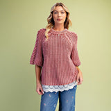 Model wearing a classic rust‑hued knit sweater with delicate lace detailing along the bottom hem.