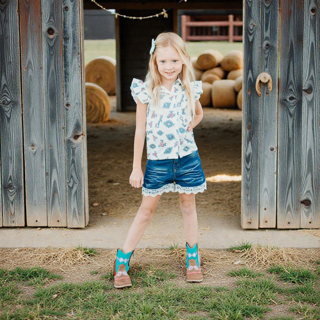 Girl wearing a vintage‑inspired cowgirl short‑sleeve shirt with bold blue accents, standing in front of a barn.