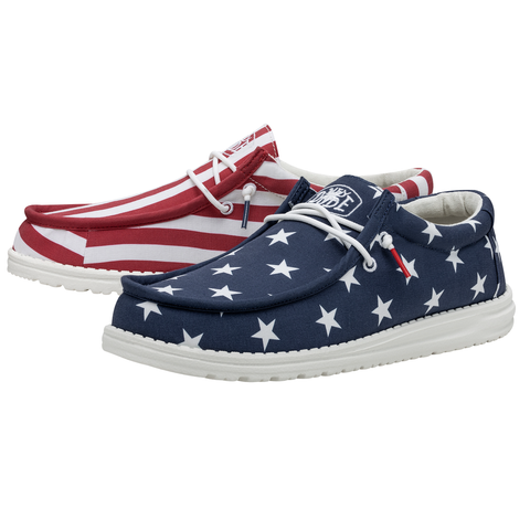 A pair of HEYDUDE shoes that feature the American flag. One of the shoes is blue with white stars, while the other one consists of red & white strips.